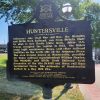 Black sign with yellow letters giving historical information about Huntersville