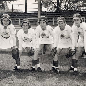 White women in baseball uniforms bent over with hands on knees