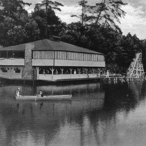 People swimming and boating in the water with multistory buildings along the shoreline