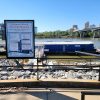 Sign saying "Arkansas Inland Maritime Museum" with boats and a river and buildings in the background