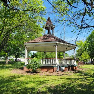 wooden gazebo on brick platform in park surrounded by trees