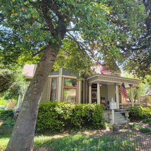 Multistory wooden gray and tan house with covered porch next to tree