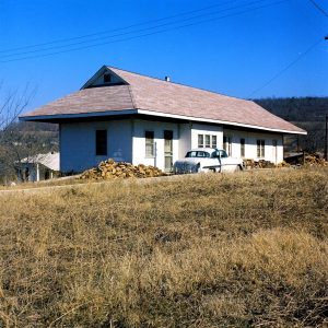 Single story white wooden house with car parked beside it