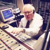 White man with glasses sitting at radio control panel