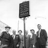 White men and women dressed in business attire standing beneath plaque