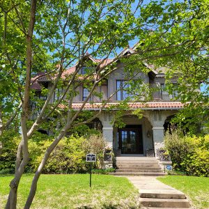 Multistory house with tile roof and covered front porch and trees in foreground