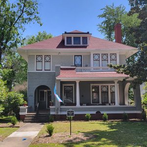 Multistory blue-gray house with red roof and porch and chimney