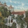 Ornate white stone multistory building with red tiled roofs with a smaller but similar-looking building in front