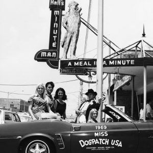 White men and white women in costume riding in convertible in front of a diner-type building