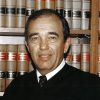 White man in tie and judge's robe standing in front of books