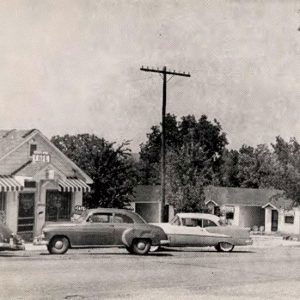 Several small buildings with striped awnings with cars parked about