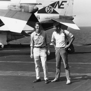 Two white men standing near a plane on board a ship