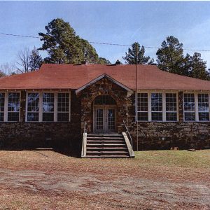 one-story rock school building with windows in front and red shingle roof