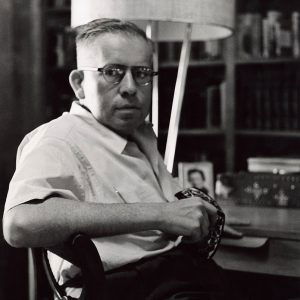 White man wearing glasses in shirtsleeves sitting at desk