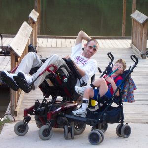 Two white people in wheelchairs posing on a boat dock