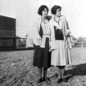 Two white women standing together in the middle of a dirt road