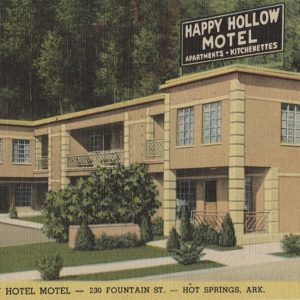 Two-story square building with multi-pane windows and sign on top saying "Happy Hollow Motel Apartments Kitchenettes"