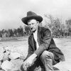 White man in jacket and hat kneeling among rocks