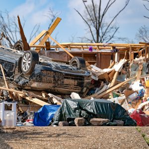 Debris including an upside down vehicle with remains of house in background