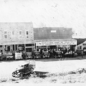 People and cars in front of a row of wooden buildings