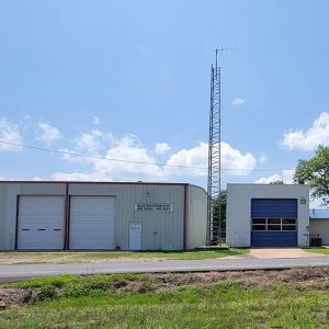 metal building with bays and low white building with a blue bay with tall antenna behind them