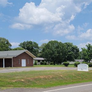 Single story red brick church building with three white crosses in the ground