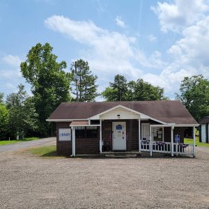 Single story red brick building with sign saying "Library" with large parking lot