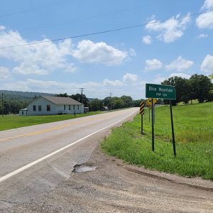 Highway with white building on one side and green sign "Blue Mountain"