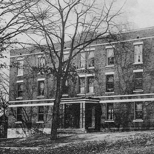 Multistory brick building with covered entrance behind denuded trees