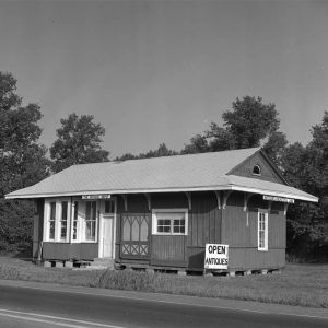 Small single story wooden buiding beside the road with sign saying "Open. Antiques."