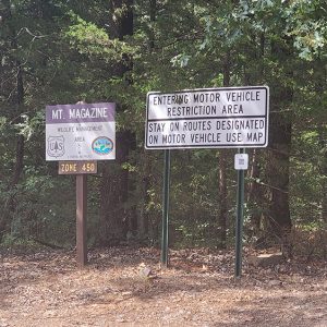 two signs in front of trees reading "Mount Magazine Wildlife Management Area" and "entering motor vehicle restriction area"