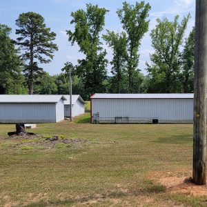 Three small white metal buildings with trees in background