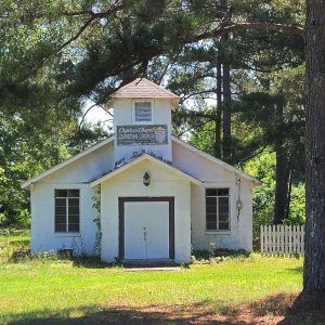 Single story white concrete block church building with bell tower amid trees