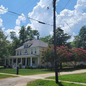 Multistory yellow wooden house with large front porch surrounded by trees