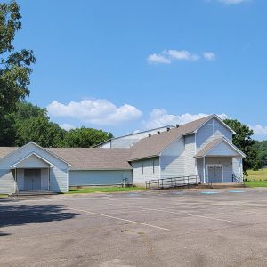 Multistory wooden white church building with single-story section and parking lot