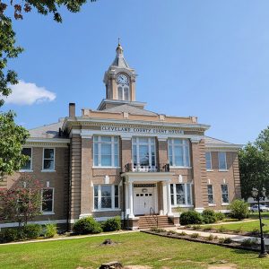 Multistory tan brick building with clock in tower and words across front of building saying "Cleveland County Court House"