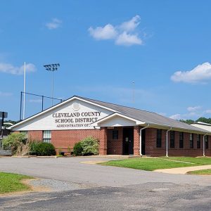 Single-story red brick building with corrugated metal buildings behind it "Cleveland County School District"