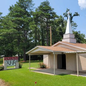 Tan brick church building with steeple with a cross at the top