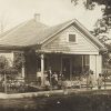 Single story white wooden house with more than a dozen white children sitting and standing