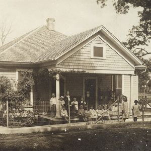 Single story white wooden house with more than a dozen white children sitting and standing