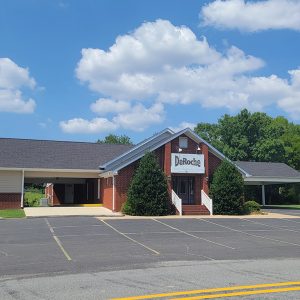 Single story red brick church building with steps leading to entrance and large parking lot