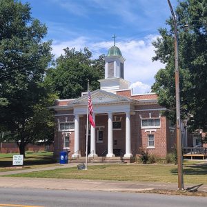 Multistory red brick building with white cupola with a cross on top and four columns in the front