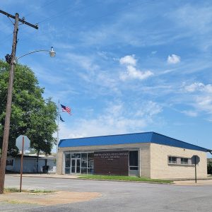 Single story tan brick building with blue roof at intersection