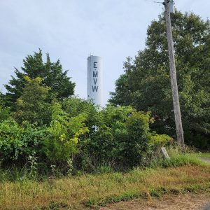 White cylindrical tower with lettering "E M V W" and trees in foreground