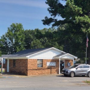 Single story orange brick post office building with parking lot