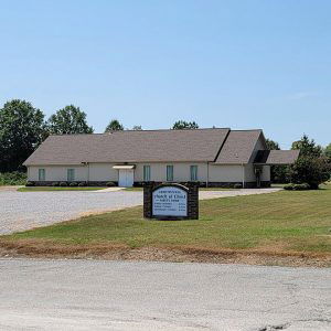 Tan church building with peaked roof and parking lot