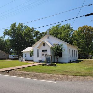 Single story white wooden church building with tall windows and a cross on top