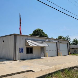 Single story beige metal building with two garage doors and an entrance door