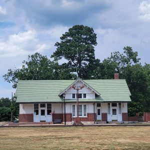 Single story white wooden building with green roof with railroad tracks in front