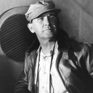 white man in leather jacket and cap with binoculars around his neck